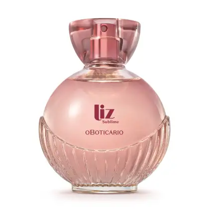 frasco de item de perfumaria da marca Liz Sublime, com embalagem de vidro arredondada rosa-claro facetado e nome da marca em vermelho escuro gravado no vidro. A tampa é em acrílico transparente e permite ver a tampa borrifadora de tom metálico rosa.