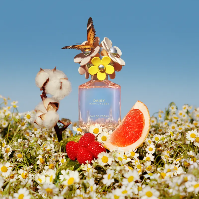 Frasco de perfume rosa da linha Daisy Marc Jacobs, com tampa decorada com flores amarelas e brancas. Rótulo com o nome da fragrância "Daisy Marc Jacobs Eau So Fresh" em letras douradas.