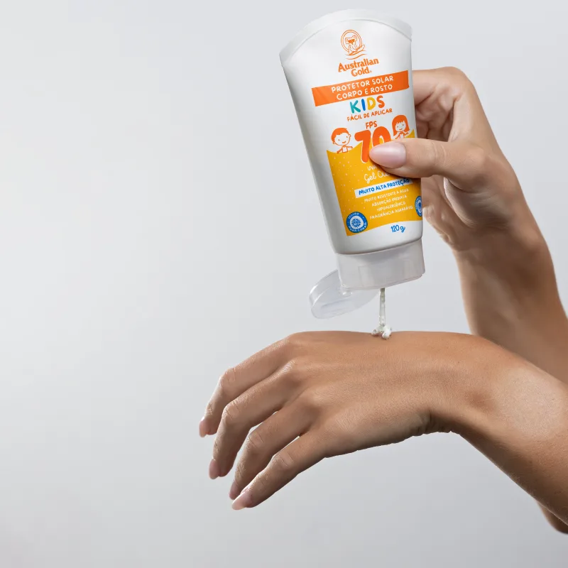 Tubo com aproximadamente 100g de produto sendo segurado por uma mão feminina. Cores vibrantes e design voltado para o público infantil.