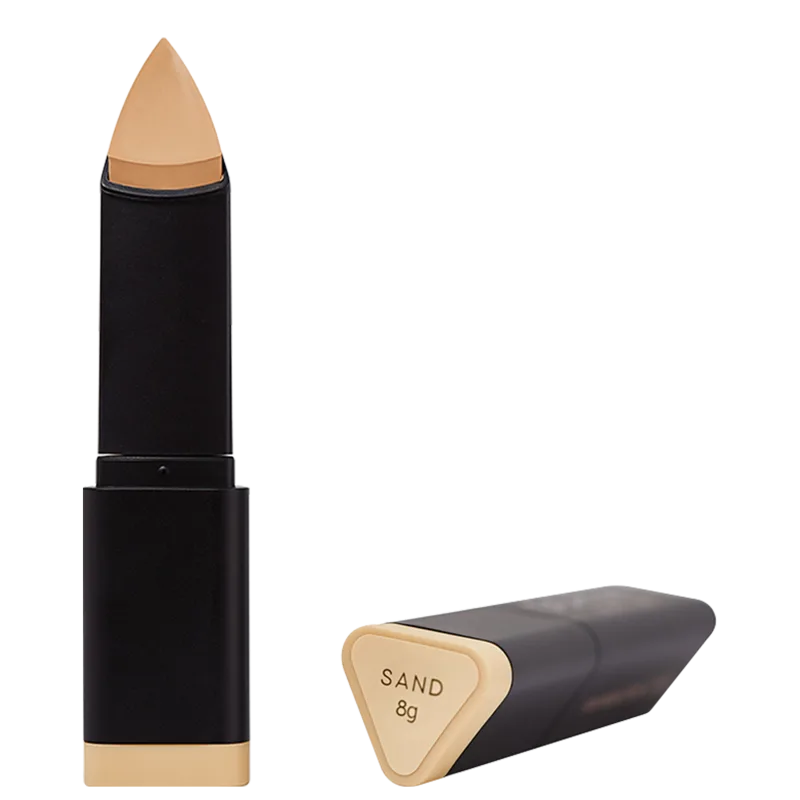 A imagem mostra detalhe da embalagem e da base Océane Edition Foundation Stick no tom Sand que possui uma ponta cônica na cor bege. As cores predominantes são preto, bege e dourado.