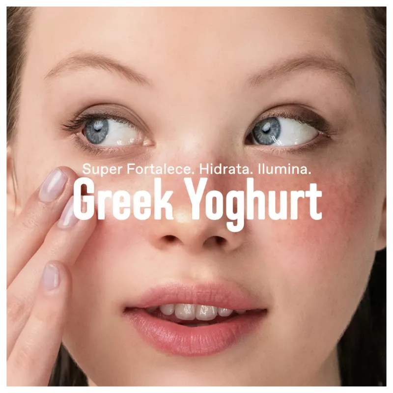 A imagem mostra um close-up do rosto de uma mulher, com seus olhos azuis e lábios rosados em destaque. O texto "Super Fortalece. Hidrata. Ilumina. Greek Yoghurt" está sobreposto na imagem, sugerindo que o iogurte grego é um ingrediente chave.