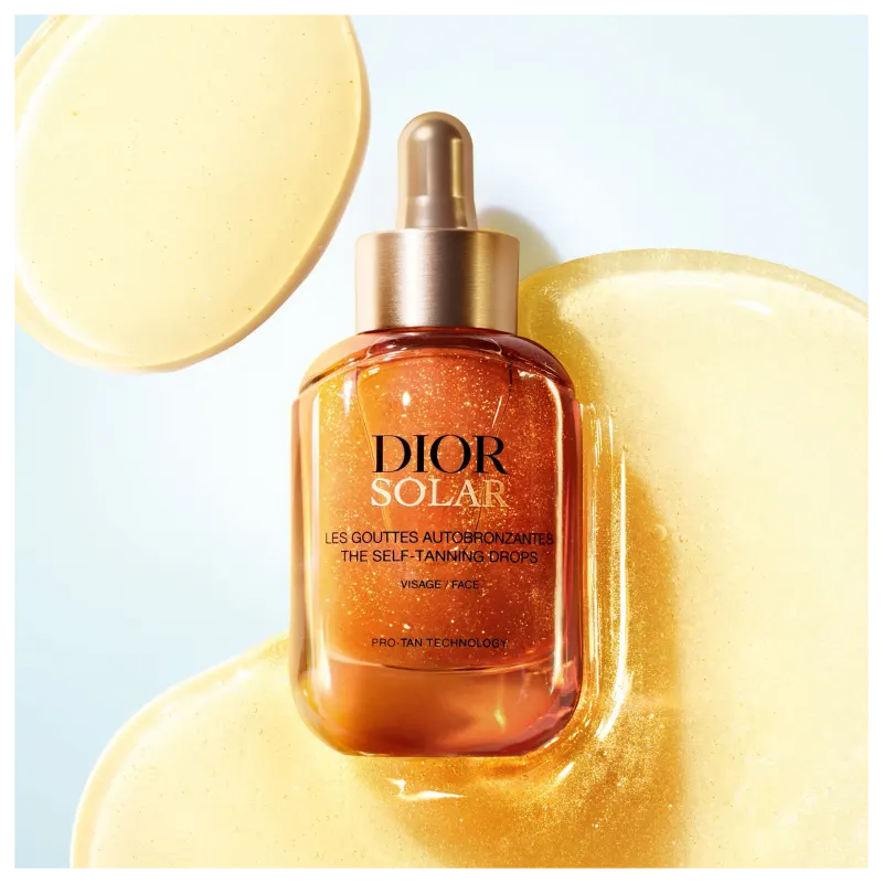 Frasco de vidro com conta-gotas dourado contendo um líquido alaranjado brilhante, rotulado como "DIOR SOLAR - The Self-Tanning Drops" em fundo branco e dourado.