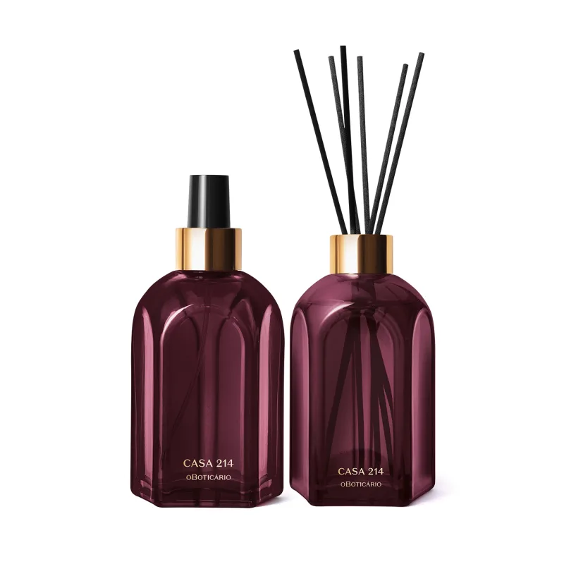 A imagem mostra dois vidros retangulares roxos, com rótulo em dourado. Um deles é o aromatizador de ambientes com válvula spray preta e o outro é um difusor com tampa dourada que acompanha varetas de madeira. Ambos são a linha Casa 214 Figo Magnífico.