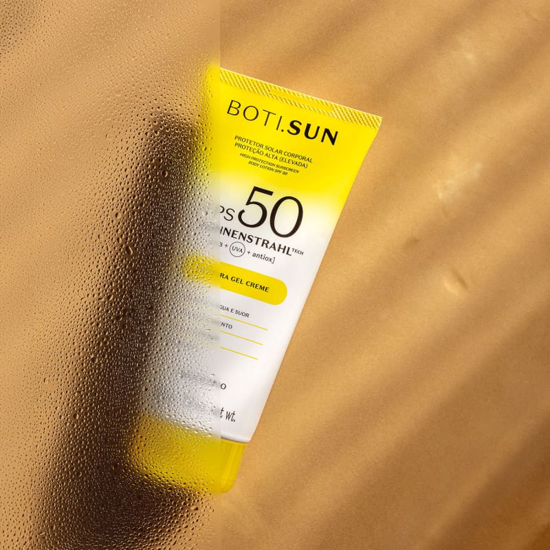 Bisnaga amarela e branca com tampa amarela e letras pretas contendo 200g de protetor solar corporal FPS 50 da marca Boti.Sun em um fundo bege com sombras onduladas.