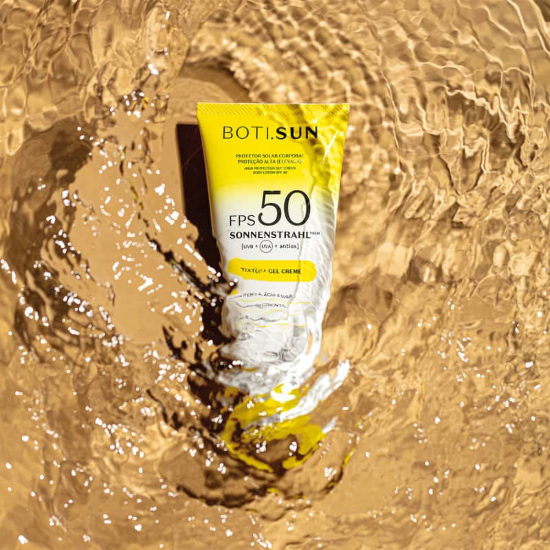 Bisnaga amarela e branca com tampa amarela e letras pretas de protetor solar corporal FPS 50 da marca Boti.Sun em um cenário d areia de praia molhada.