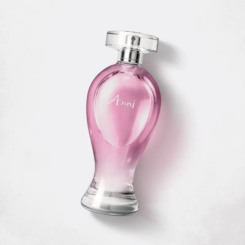 Vidro transparente em formato curvilíneo com líquido rosa, pulverizador prateado e tampa transparente contendo 200ml de desodorante colônia Boticollection Anni em um fundo cinza.