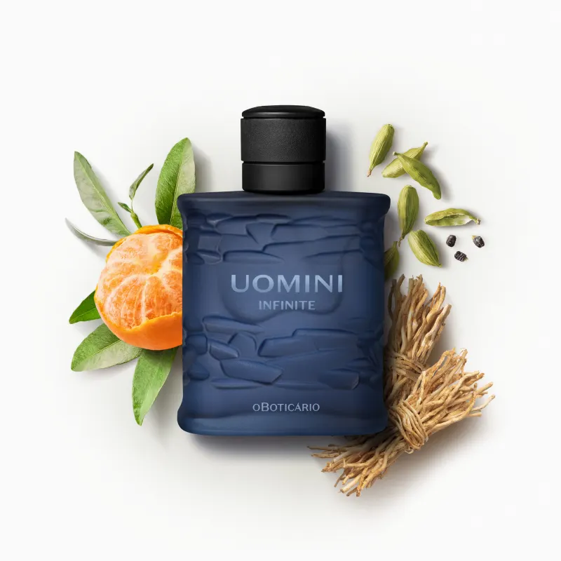 Frasco retangular azul marinho com texturas onduladas, tampa preta e letras com degradê em tons de azul de desodorante colônia da marca Uomini Infinite rodeado por gomos de bergamota, folhas verdes, vagens de cardamomo e raízes secas.