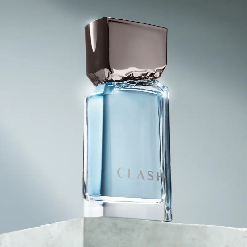 Frasco de item de perfumaria da marca Clash sobre superfície de mármore branco, com fundo desfocado em tons de azul e cinza.
