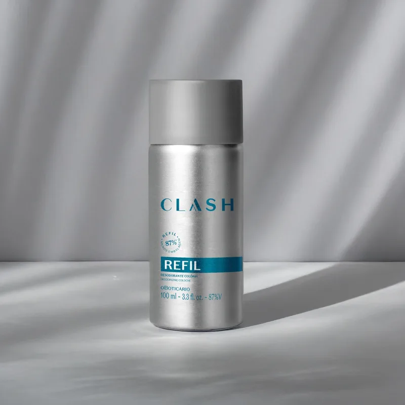 Embalagem prateada de item de perfumaria da marca Clash sobre superfície cinza, com iluminação cenográfica suave e sombras projetadas.