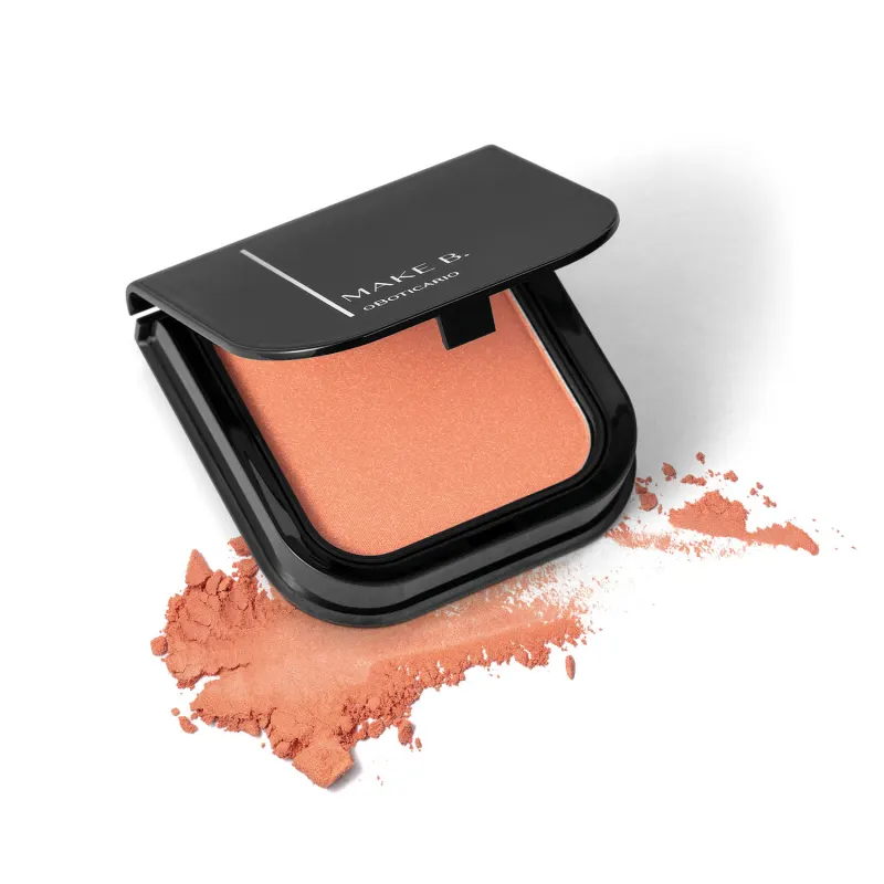 Blush em pó mate Luminoso Coral Make B. na cor coral em estojo quadrado preto de cantos arredondados com espelho na tampa. Um pouco do produto está esfarelado ao lado da embalagem.