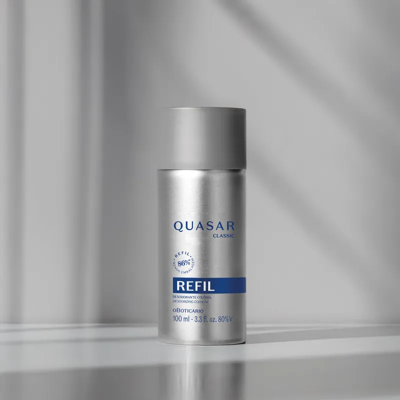 Refil de desodorante colônia Quasar Classic em frasco prateado com detalhes e letras azuis em fundo em tons de cinza com luzes naturais.