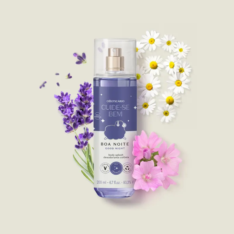 Frasco com líquido azul claro, pulverizador prateado, tampa transparente e rótulo azul escuro e branco com ovelhinha ilustrada de body splash da marca Cuide-se Bem Boa Noite em meio a flores e folhagens roxas e brancas sobre superfície clara.