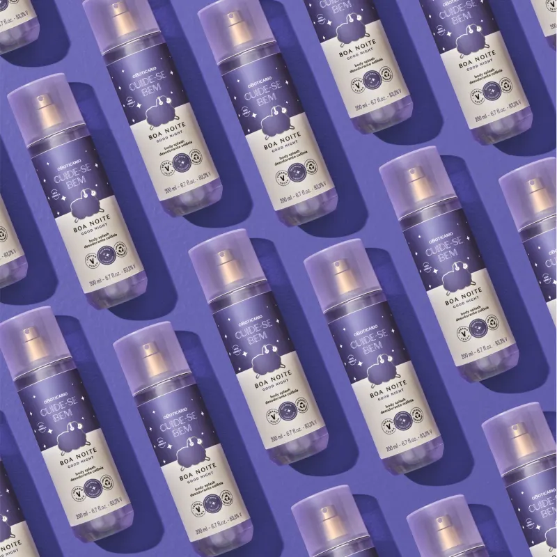 Diversos frascos com rótulos azuis e brancos contendo body splash da marca Cuide-se Bem Boa Noite dispostos lado a lado em um fundo azul escuro.