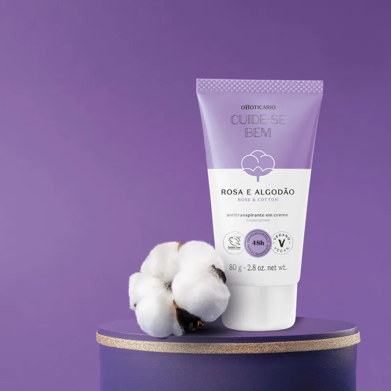 Bisnaga em tons de lilás e branco com flor de algodão ilustrada contendo 80g de antitranspirante em creme da marca Cuide-se Bem Rosa e Algodão. Ao lado da embalagem há flores de algodão e tudo está em superfície e fundo azul escuro.