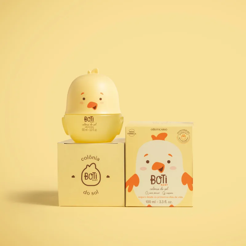 Frasco em formato de passarinho amarelo com parte superior na cor bege escuro e detalhes laranjas de colônia do sol da marca Boti Baby em cima de uma caixa com o nome da marca e ao lado da caixa do produto com ilustração de passarinho.