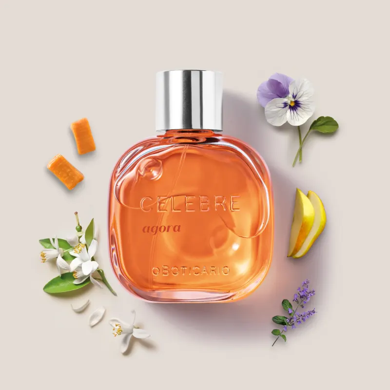 Frasco de vidro transparente com líquido laranja, tampa prateada e letras pretas e em relevo contendo de desodorante colônia Celebre Agora Feminino, rodeado por caramelos, violeta, flor de laranjeira e peras frescas.
