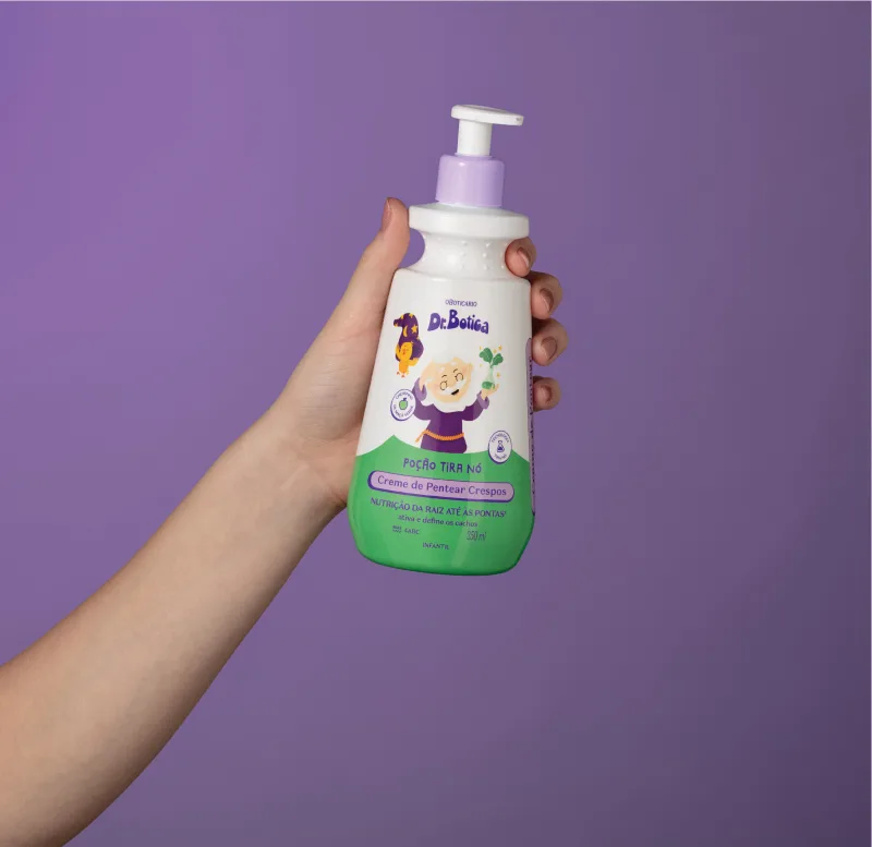 Imagem de uma mão segurando uma embalagem branca e verde com válvula dosadora roxa de creme de pentear infantil para cabelos crespos da marca Dr. Botica em fundo azul escuro.
