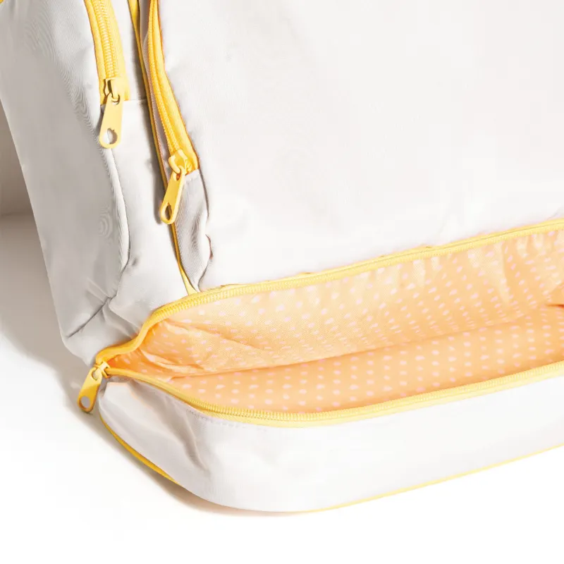 Close-up de Mochila branca com detalhes em amarelo com bolso frontal do fundo da mochila aberto revelando um revestimento amarelo de bolinhas brancas.