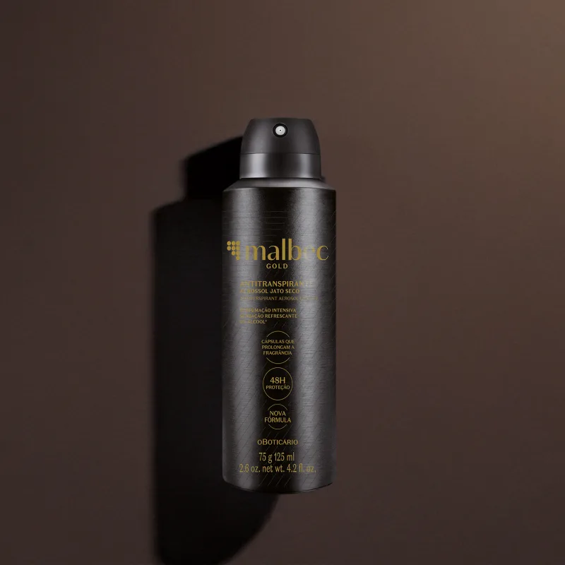 Imagem de um frasco preto de desodorante antitranspirante aerossol da marca Malbec Gold, com rótulo em dourado. Ele está em um fundo cinza escuro e há uma sombra, compondo um cenário forte e elegante.
