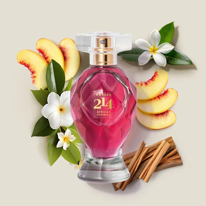 Vidro lapidado com líquido rosa, tampa transparente, pulverizador e letras douradas de Eau de Parfum Botica 214 African Sunrise Floral Frutal em meio a fatias de pêssego, folhas verdes, flores brancas e varas de canela em cenário claro e natural.