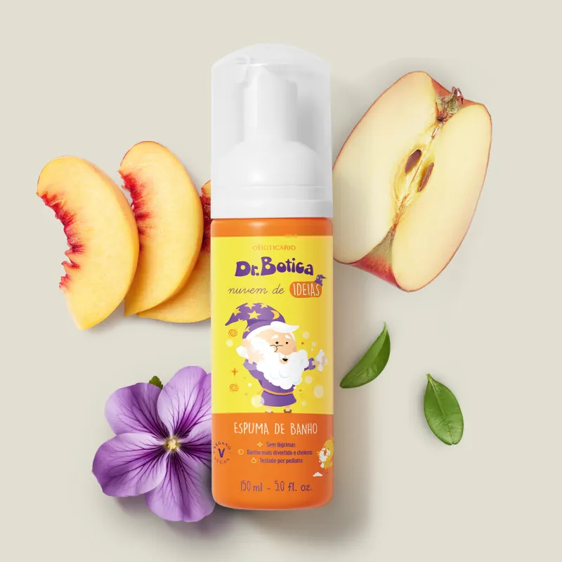 Espuma de banho corporal Nuvem de Ideias Dr. Botica em frasco com tampa branca e rótulo amarelo e laranja com ilustração do personagem da marca sobre superfície clara, com fatias de pêssego, maçã e flor roxa ao redor, em cenário minimalista e natural.