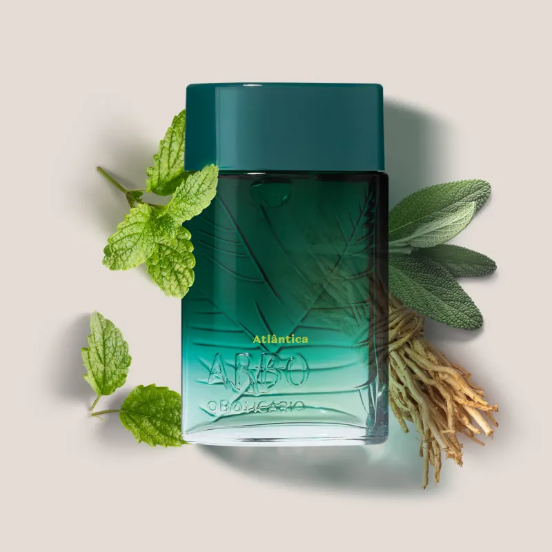 Frasco de desodorante colônia Arbo Atlântica, com design verde degradê e textura de folhas, apresentado com folhas de hortelã e raízes secas.