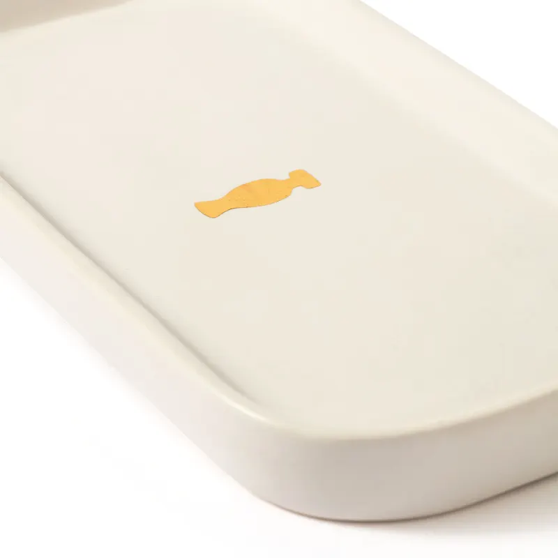Bandeja para lavabo branca da marca Casa 214 no formato retangular com cantos arredondados e com logo do Boticário em dourado no centro.