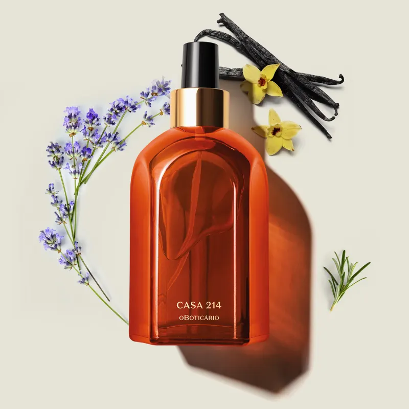 Vidro laranja de tampa spray preta com detalhe e letras douradas contendo aromatizador de ambientes Casa 214 Vanilla Sublime em ambiente com flores de lavanda e narciso, sobre superfície clara.