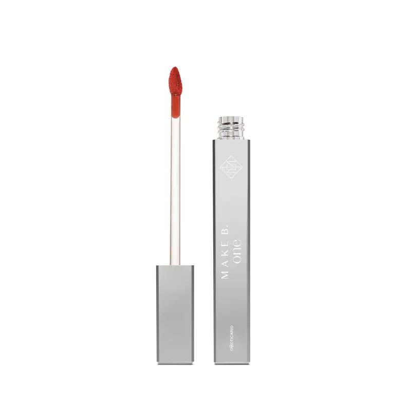 Frasco de batom líquido vermelho Deep Carmine da marca Make B. One Velvet Sublime em embalagem prateada com haste branca, esponja aplicadora na cor do batom e nome da marca gravada.