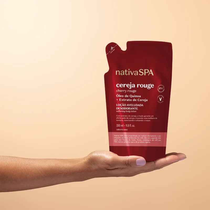 Mão feminina com unhas pintadas segurando um refil de loção aveludada corporal da marca Nativa SPA Cereja Rouge em sachê vermelho escuro, letra brancas e detalhe rosa em fundo rosa claro.