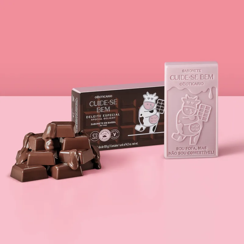 Sabonete em barra de chocolate com embalagem especial. Embalagem marrom com ilustração de uma vaca usando um avental e segurando uma barra de chocolate. Sabonete com ilustração de uma vaca e texto "Sou fofa, mas não sou comestível!".