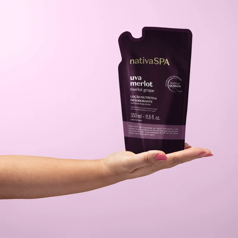 Refil na cor roxa de loção hidratante corporal da marca Nativa SPA Uva Merlot, segura por mão feminina com esmalte rosa, sobre fundo rosa claro.