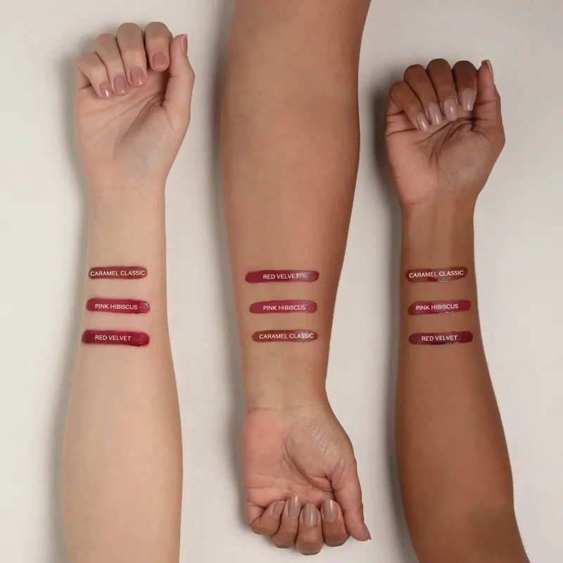 Imagem mostra três braços de cores diferentes estendidos sobre superfície branca sendo o braço mais a direita de pele negra, o do meio de pele parda e o da esquerda com pele branca, todos com diversos tons de batom aplicados sobre eles e seus códigos.