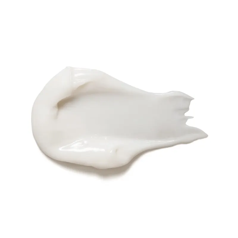 Imagem da textura cremosa e brilhante da máscara capilar, com cor branca, lisa, em quantidade moderada sobre fundo também branco.