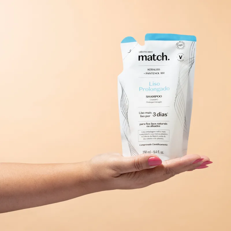 Mão segurando um refil de shampoo Match Liso Prolongado em sachê nas cores rosa e branca com letras pretas em fundo em tons de rosa.