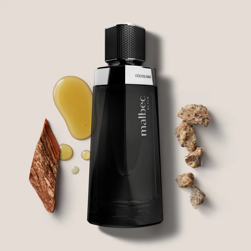 O frasco é preto e possui um design moderno e elegante. Ao redor do frasco, há alguns elementos decorativos, como pedras, madeiras e uma substância líquida amarelada, que parecem ser ingredientes naturais utilizados na composição da fragrância.