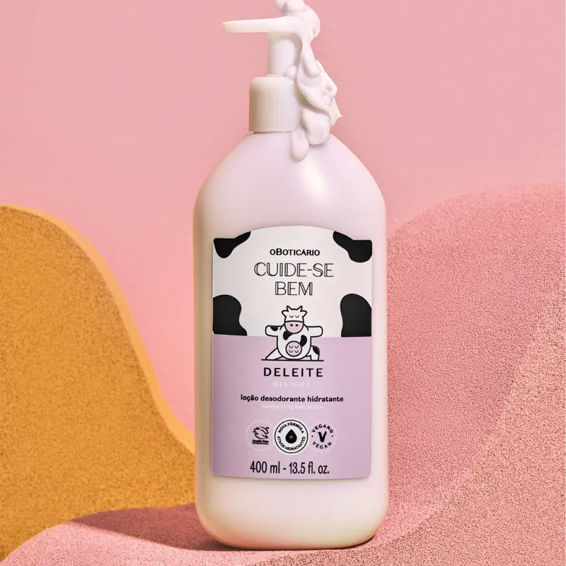 Embalagem branca com rótulo rosa e branco e ilustração de vaca de loção hidratante corporal Cuide-se Bem Deleite sobre superfície rosa e amarela com formas geométricas.