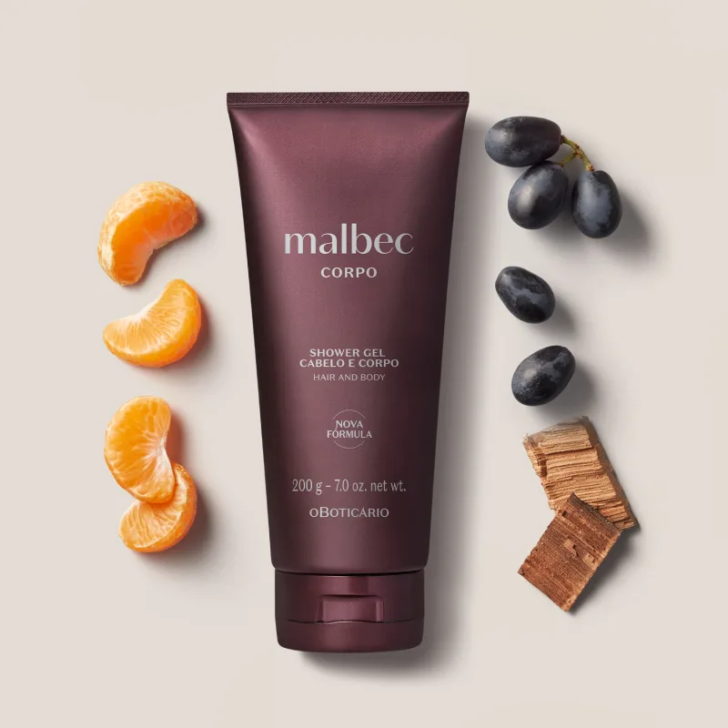 Imagem de um tubo de gel de banho e cabelo da marca Malbec, sobre superfície clara com laranjas e uvas pretas ao redor, em ambiente minimalista e neutro.