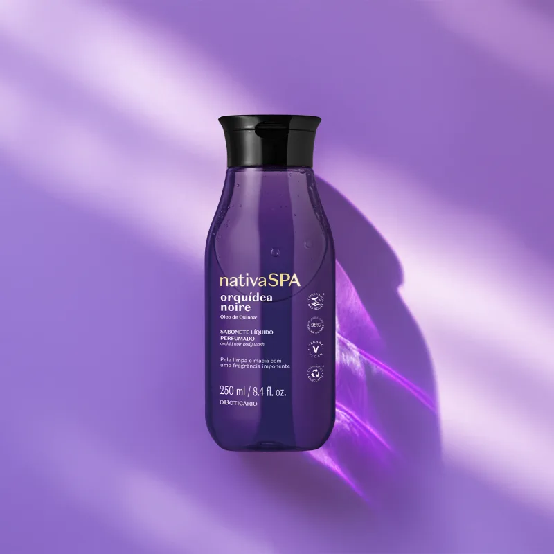 A imagem mostra um frasco de sabonete líquido perfumado Nativa SPA Orquídea Noire, na cor roxa, tampa preta e com rótulo destacando o nome e informações sobre o produto em letras douradas. Ele está à frente de um fundo azul com luzes brancas.