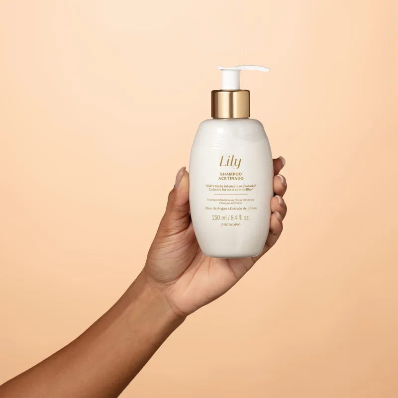 Imagem de embalagem branca de shampoo da marca Lily com tampa dourada e bomba dosadora, segurada por mão em fundo branco e laranja claro.