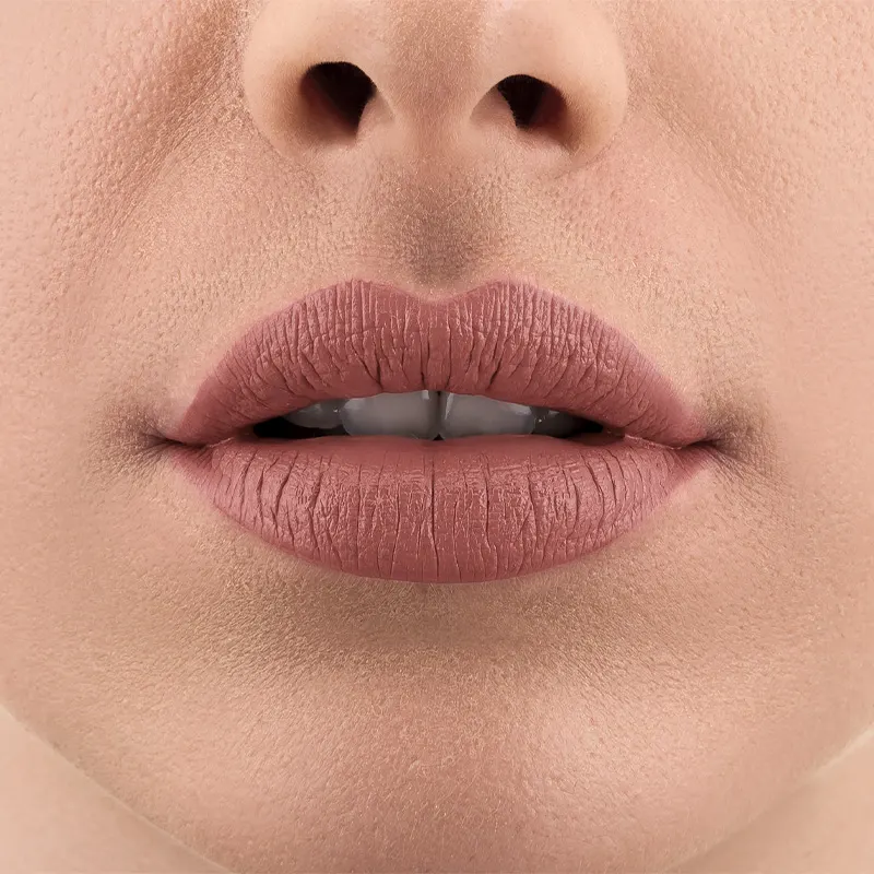 Imagem de um rosto feminino em close-up, evidenciando os lábios com o batom líquido Make B. na cor rosa. A boca está entreaberta mostrando parcialmente os dentes brancos.