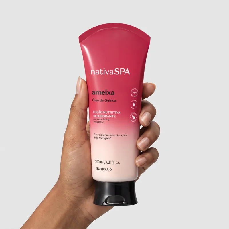 Bisnaga de loção corporal Nativa SPA em degradê de vermelho para o branco sendo segurada por mão feminina negra, mostrando a frente da embalagem sobre fundo branco.