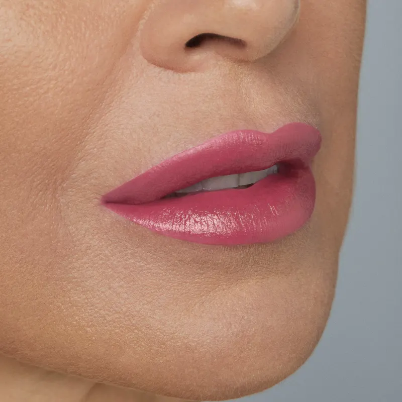 Boca feminina de mulher branca em close mostrando queixo e um pedaço do nariz, com lábios entreabertos mostrando ligeiramente os dentes brancos com batom rosado brilhante.