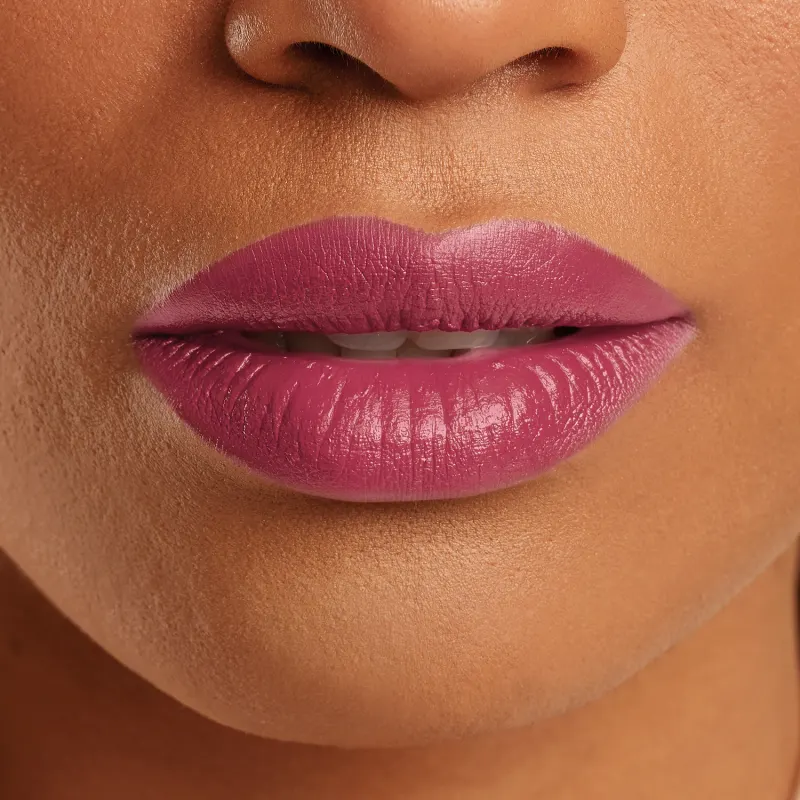 Boca feminina de mulher parda em close mostrando queixo e um pedaço do nariz, com lábios entreabertos mostrando ligeiramente os dentes brancos com batom rosado brilhante.