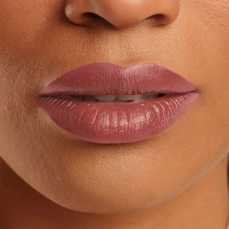 Boca feminina de mulher branca em close mostrando queixo e um pedaço do nariz, com lábios levemente entreaberto, revelando um pouco dos dentes frontais brancos e lábios com batom rosado sobre eles.