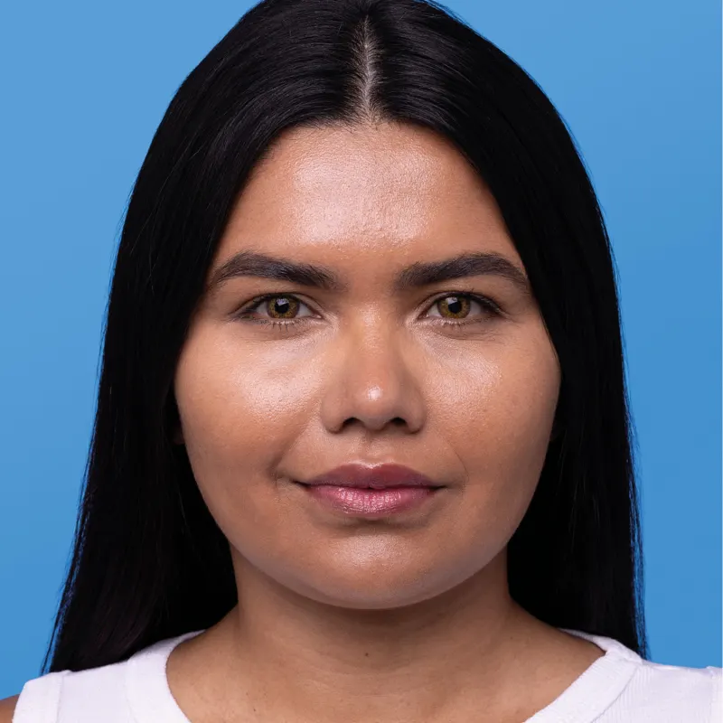 Imagem mostra rosto de mulher com cabelo escuro liso e comprido  sobre fundo azul, mostrando o resultado final após uso de protetor solar com cor.