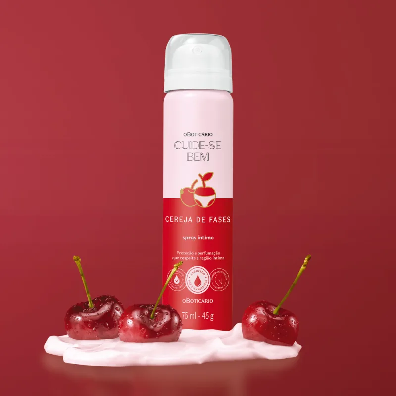 Imagem de frasco de spray íntimo desodorante da marca Cuide-se Bem Cereja De Fases. A embalagem é rosa e vermelha e está em um cenário de fundo vermelho com um creme branco na superfície e cerejas vermelhas frescas espalhadas sobre ele.