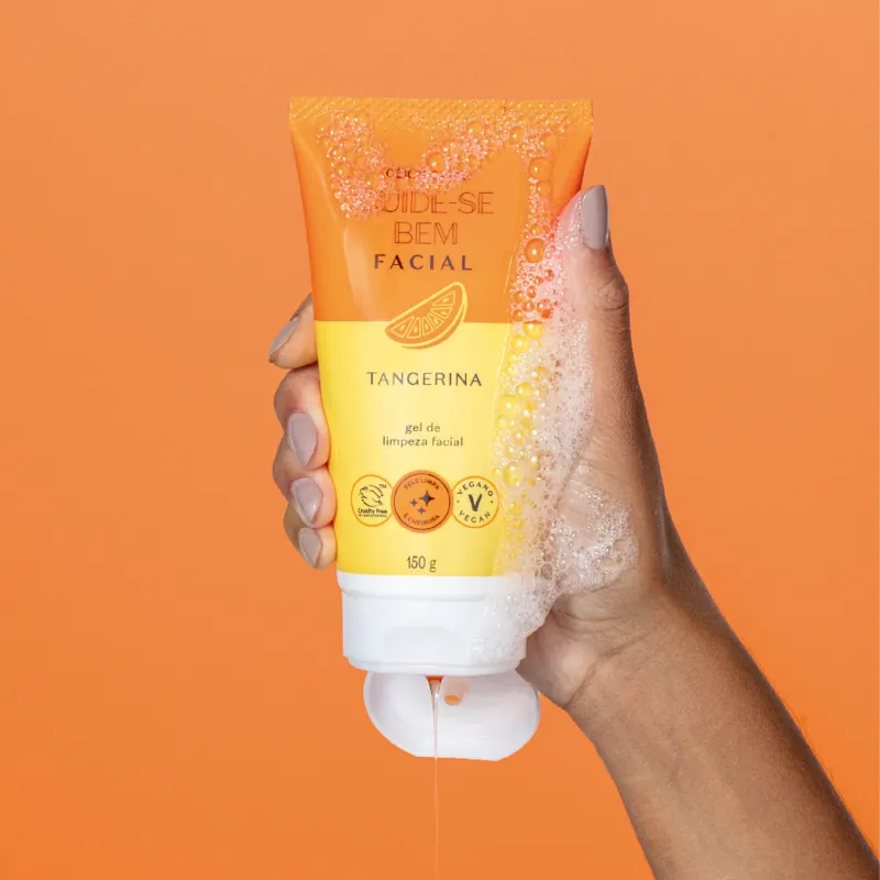 Imagem do tubo de gel de limpeza facial da marca Cuide-se Bem Tangerina em fundo laranja, sendo segurado por mão feminina com unhas pintadas de tom claro. A embalagem é laranja e amarela e possui tampa branca.