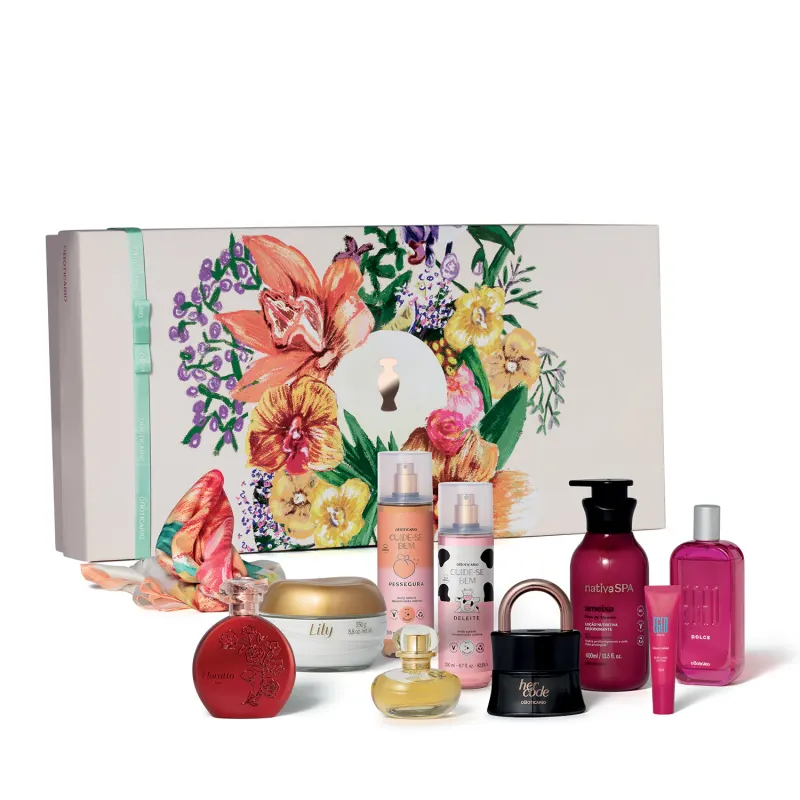 A imagem mostra um kit de presentes contendo uma caixa branca com ilustrações florais, seguida de diversos produtos de perfumaria e cuidados pessoais do Boticário, incluindo frascos, potes e bisnagas em cores variadas.