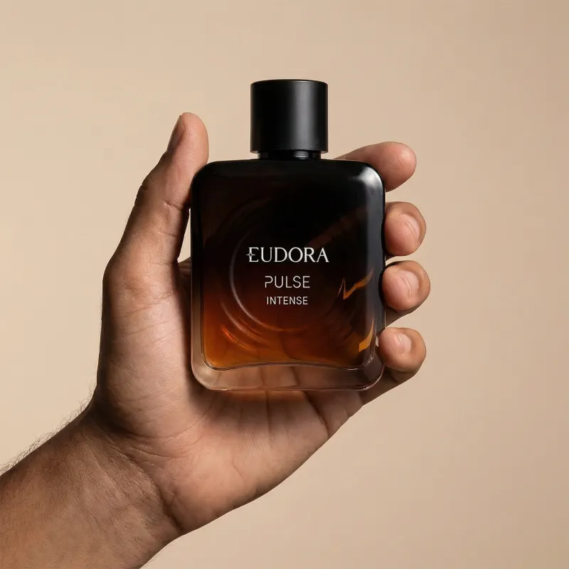 Imagem de um frasco do desodorante colônia da marca Eudora Pulse Intense, em um fundo bege claro. O produto é segurado por uma mão masculina.